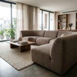 Canapé panoramique en bouclé taupe au centre d'un salon contemporain avec sol en béton poli et grandes fenêtres