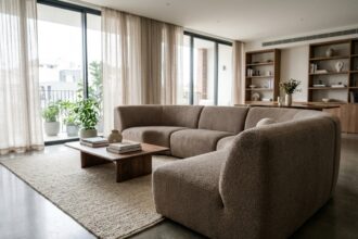 Canapé panoramique en bouclé taupe au centre d'un salon contemporain avec sol en béton poli et grandes fenêtres