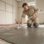 Ouvrier étalant une chape autonivelante sur un plancher chauffant avec tube PEX visible lors d'une rénovation intérieure