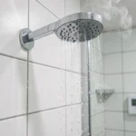 Pomme de douche chromée de type pluie avec eau coulant sur carrelage blanc dans une salle de bain moderne